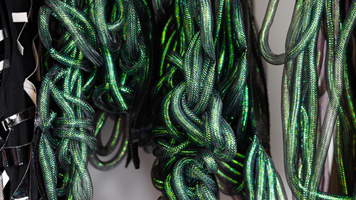 Green iridescent tubing is knotted and woven into neckpieces to represent particles colliding in a supernova.